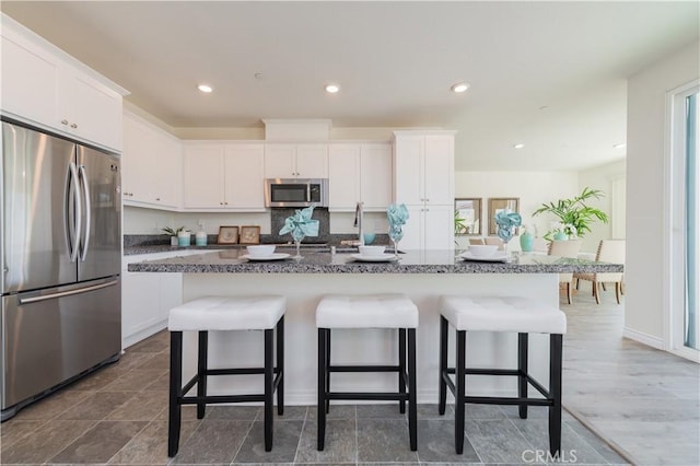 kitchen with a center island with sink, stainless steel appliances, a kitchen bar, and white cabinetry