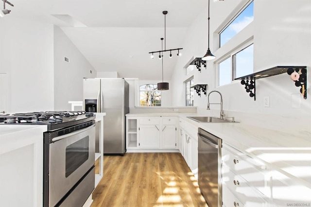 kitchen with sink, white cabinets, light hardwood / wood-style flooring, pendant lighting, and appliances with stainless steel finishes