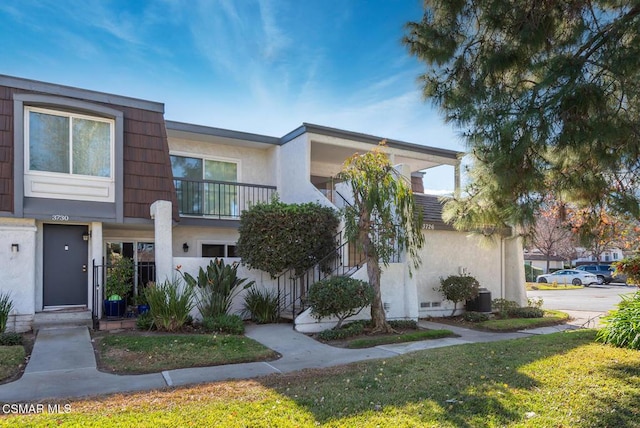 view of front of property with central AC unit, a front lawn, and a balcony