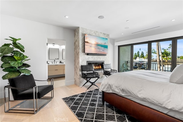 bedroom featuring light hardwood / wood-style floors, access to exterior, sink, ensuite bathroom, and a tile fireplace