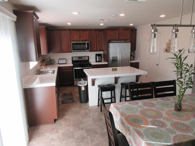 kitchen featuring a center island, sink, appliances with stainless steel finishes, a breakfast bar area, and tile counters