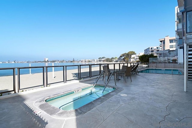 view of pool featuring a hot tub, a water view, and a patio