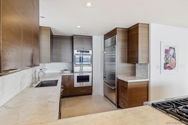 kitchen with stainless steel appliances, backsplash, dark brown cabinets, light stone countertops, and sink