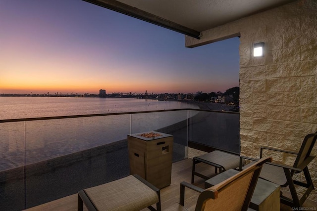 patio terrace at dusk featuring a water view and a balcony