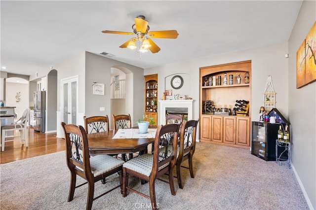 dining space with ceiling fan, light colored carpet, and built in features