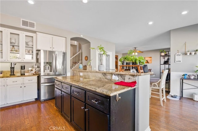 kitchen with white cabinets, a center island, stainless steel fridge with ice dispenser, light stone countertops, and dark wood-type flooring