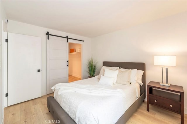 bedroom featuring a spacious closet, a closet, a barn door, and light hardwood / wood-style flooring