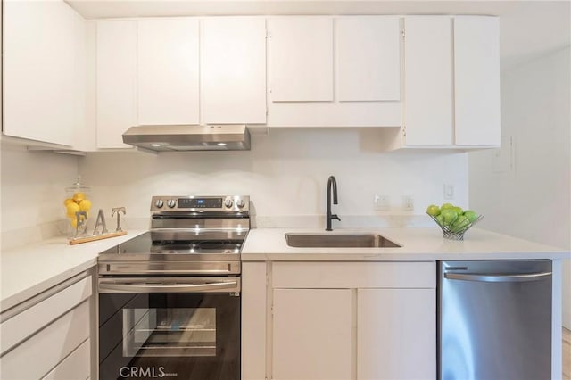 kitchen with stainless steel appliances, sink, white cabinetry, and wall chimney range hood