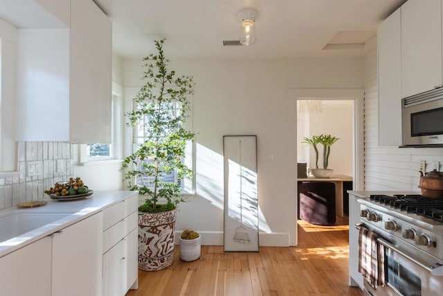 kitchen featuring decorative backsplash, white cabinetry, appliances with stainless steel finishes, and light wood-type flooring