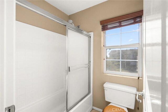 bathroom with a wealth of natural light, enclosed tub / shower combo, and toilet