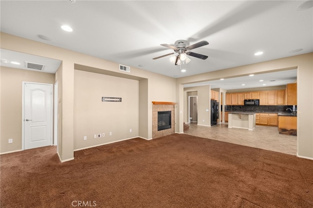 unfurnished living room featuring a fireplace, light colored carpet, and ceiling fan