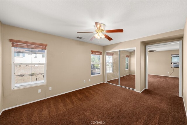 unfurnished bedroom featuring cooling unit, ceiling fan, dark carpet, and a closet