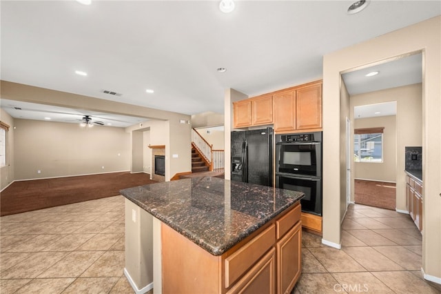 kitchen with light colored carpet, dark stone countertops, a kitchen island, ceiling fan, and black appliances