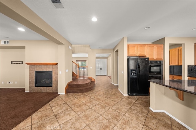 kitchen with dark stone countertops, light tile patterned floors, a tile fireplace, and black appliances