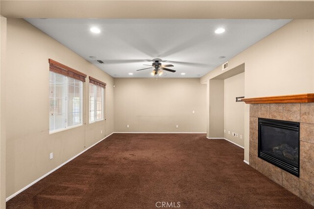 unfurnished living room with ceiling fan, dark carpet, and a tile fireplace