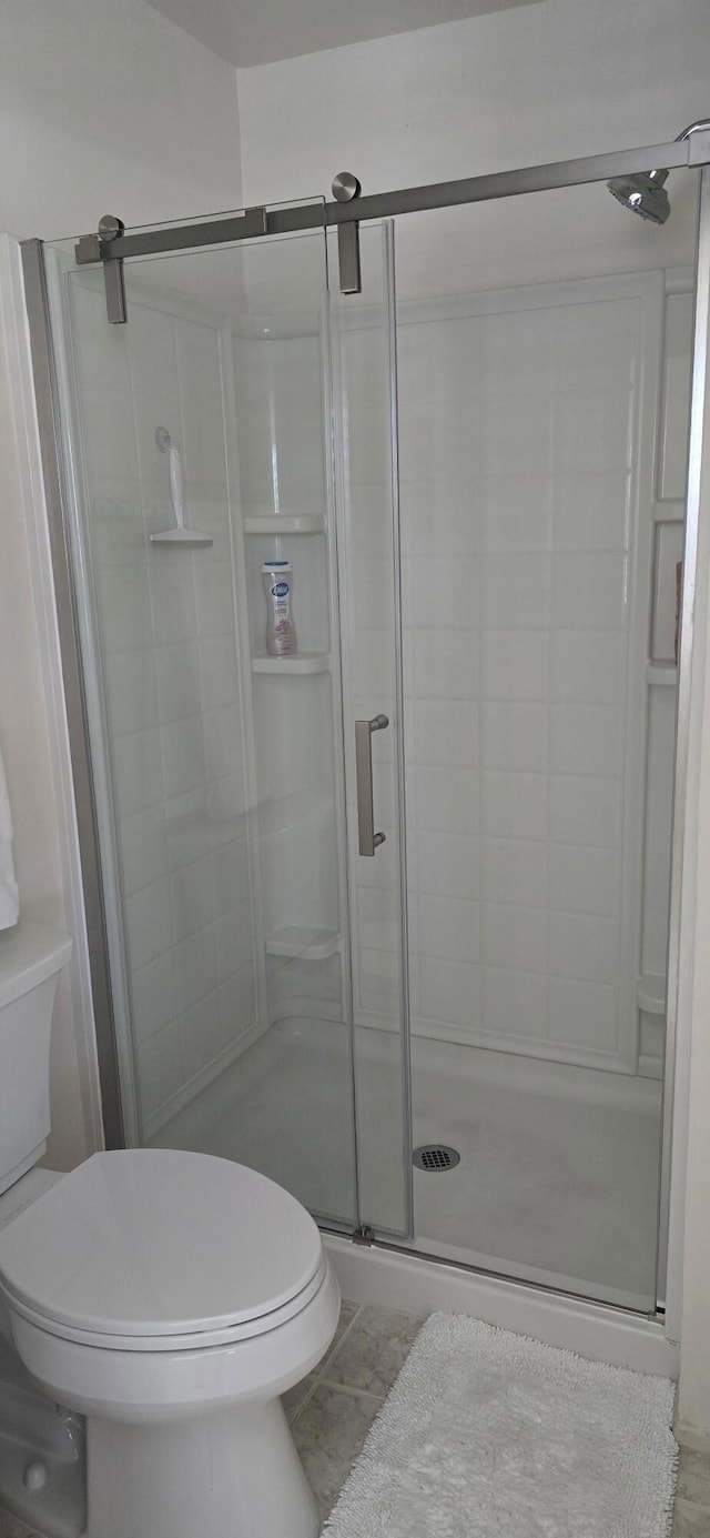 bathroom featuring toilet, tile patterned flooring, and a shower with door