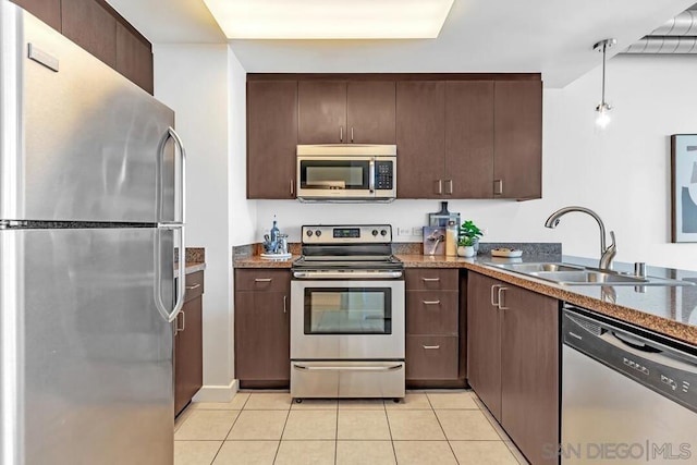 kitchen with light tile patterned floors, stainless steel appliances, decorative light fixtures, dark brown cabinets, and sink