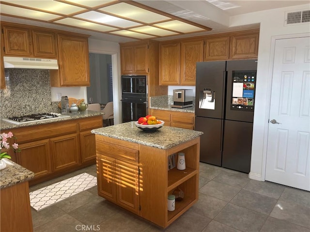 kitchen with dark tile patterned floors, black appliances, a kitchen island, decorative backsplash, and light stone counters