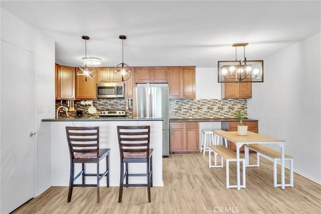 kitchen with hanging light fixtures, tasteful backsplash, stainless steel appliances, and light hardwood / wood-style flooring