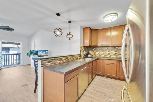 kitchen with kitchen peninsula, decorative backsplash, hanging light fixtures, stainless steel refrigerator, and sink