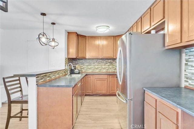 kitchen with pendant lighting, decorative backsplash, sink, stainless steel refrigerator, and light hardwood / wood-style flooring