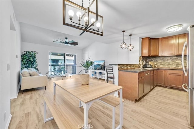 kitchen featuring ceiling fan with notable chandelier, decorative light fixtures, decorative backsplash, stainless steel fridge, and light hardwood / wood-style flooring