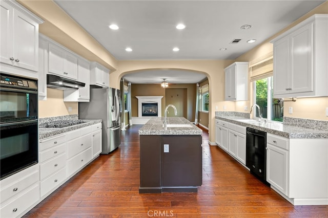 kitchen with light stone countertops, white cabinetry, black appliances, and a kitchen island with sink