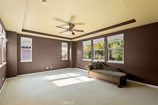 sitting room featuring ceiling fan, light colored carpet, and a raised ceiling