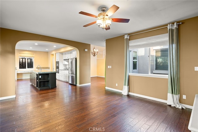 unfurnished living room with dark wood-type flooring, sink, and ceiling fan with notable chandelier