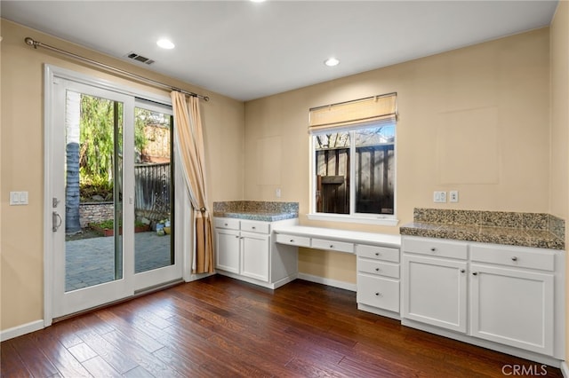 kitchen featuring dark wood-type flooring, built in desk, white cabinets, and light stone counters