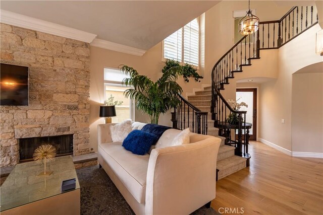 living room with a chandelier, crown molding, hardwood / wood-style flooring, and a stone fireplace