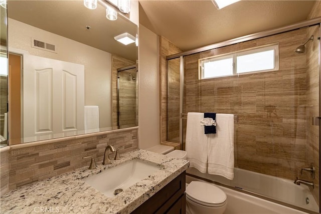 full bathroom featuring toilet, vanity, shower / bath combination with glass door, and tasteful backsplash