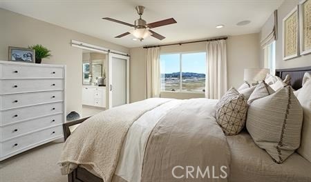 bedroom with ceiling fan, a barn door, light carpet, and ensuite bathroom