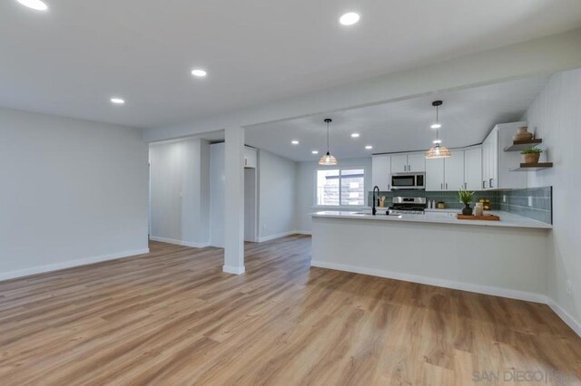 kitchen with kitchen peninsula, sink, white cabinetry, light hardwood / wood-style flooring, and appliances with stainless steel finishes