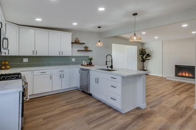 kitchen with dishwasher, kitchen peninsula, sink, white cabinetry, and hanging light fixtures