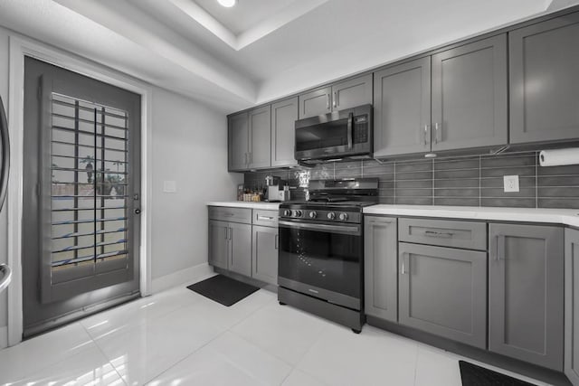 kitchen with backsplash, a raised ceiling, light tile patterned flooring, gray cabinetry, and stainless steel appliances