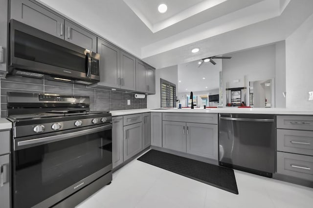 kitchen with tasteful backsplash, gray cabinets, a raised ceiling, sink, and appliances with stainless steel finishes