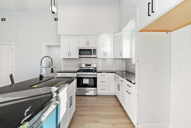 kitchen featuring white cabinetry, appliances with stainless steel finishes, backsplash, a towering ceiling, and sink