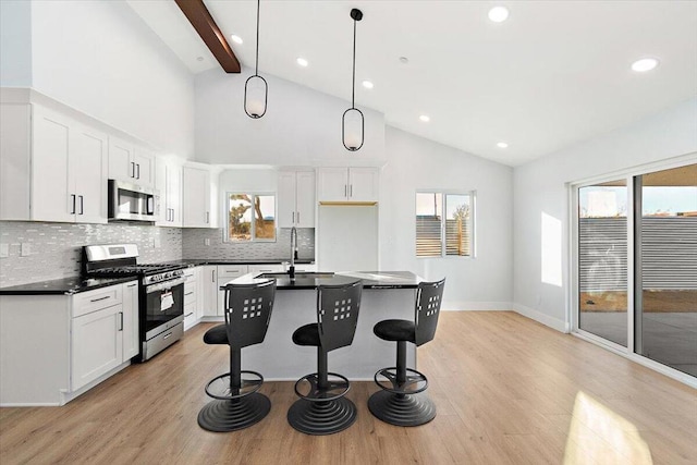 kitchen with white cabinets, appliances with stainless steel finishes, beam ceiling, and a kitchen island with sink