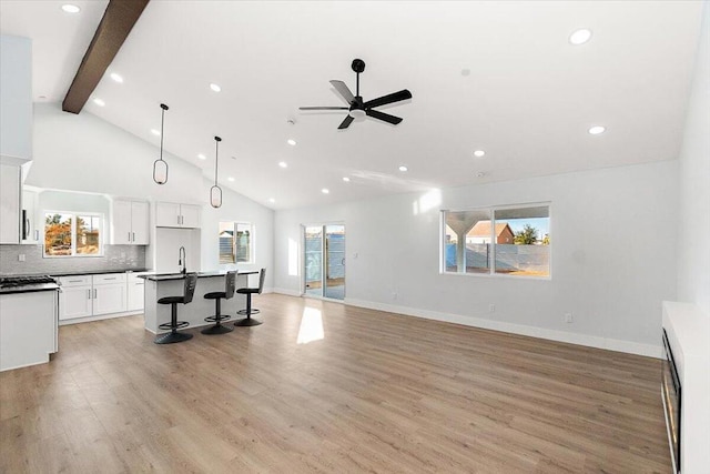 kitchen featuring pendant lighting, white cabinets, a kitchen island with sink, ceiling fan, and a breakfast bar