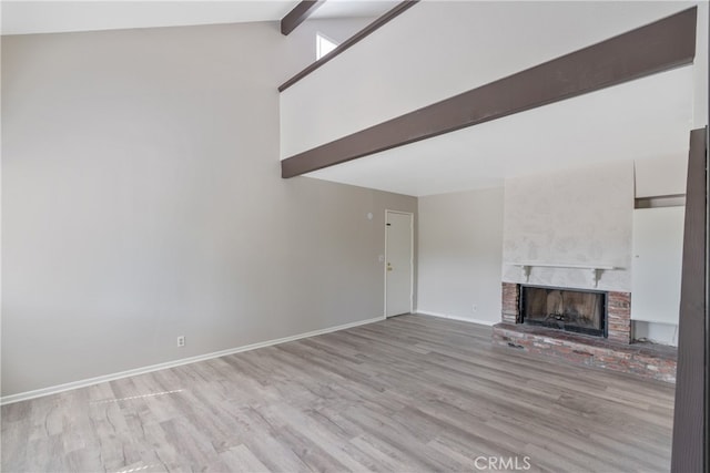 unfurnished living room with lofted ceiling with beams, a brick fireplace, and light hardwood / wood-style floors