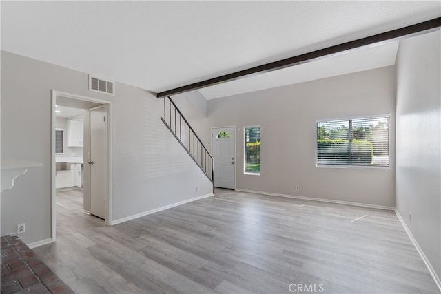 unfurnished living room featuring beam ceiling and light hardwood / wood-style floors