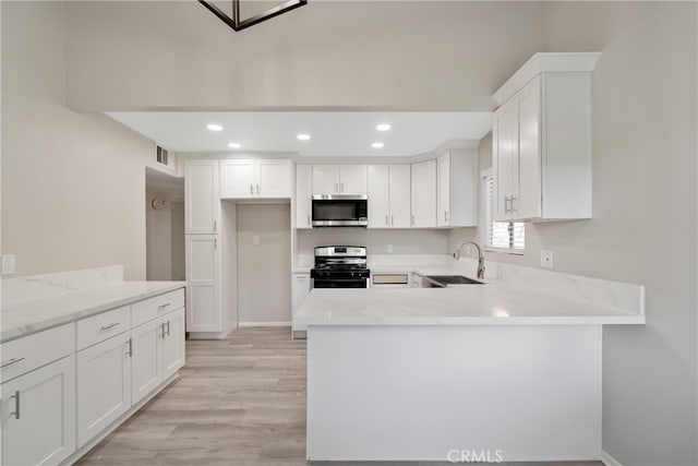 kitchen with sink, light wood-type flooring, light stone countertops, white cabinets, and range