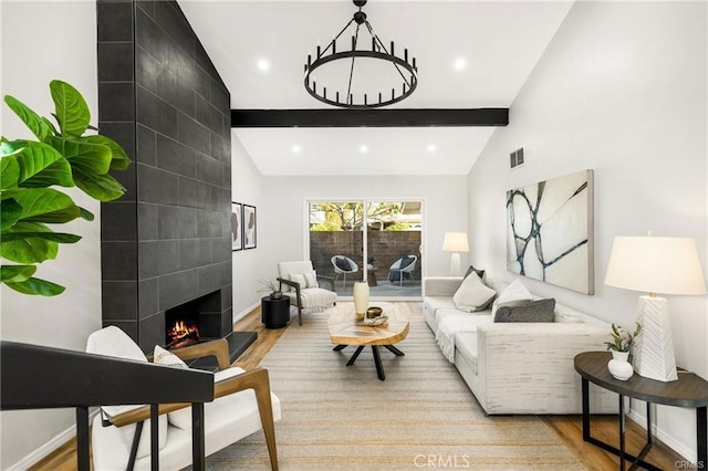 living room with vaulted ceiling with beams, a tile fireplace, and light hardwood / wood-style flooring