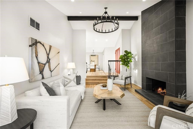 living room featuring light wood-type flooring, a tiled fireplace, and vaulted ceiling with beams