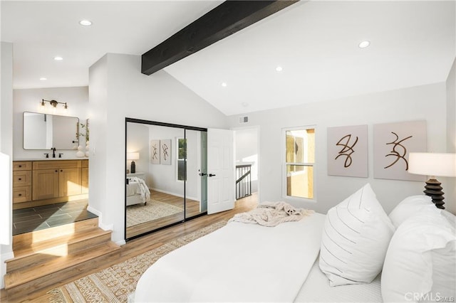 bedroom with ensuite bathroom, vaulted ceiling with beams, sink, light hardwood / wood-style flooring, and a closet