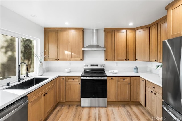 kitchen featuring light wood-type flooring, stainless steel appliances, wall chimney exhaust hood, and sink