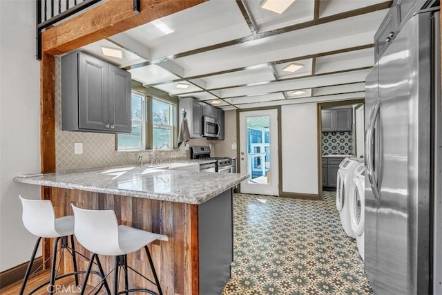 kitchen featuring kitchen peninsula, a kitchen bar, sink, stainless steel appliances, and light stone counters