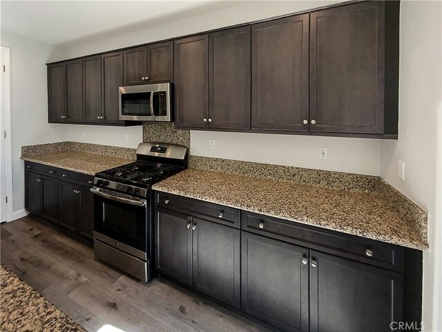 kitchen with dark brown cabinetry, light stone countertops, dark hardwood / wood-style flooring, and stainless steel appliances