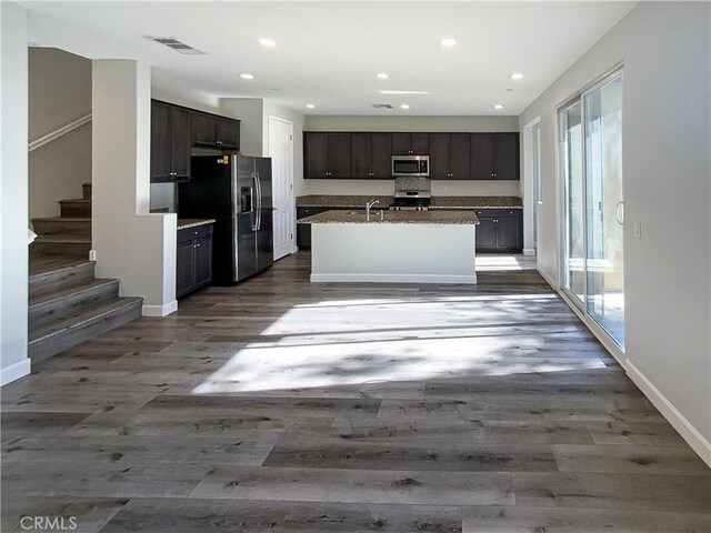 kitchen with sink, dark brown cabinets, stainless steel appliances, a center island with sink, and dark hardwood / wood-style flooring